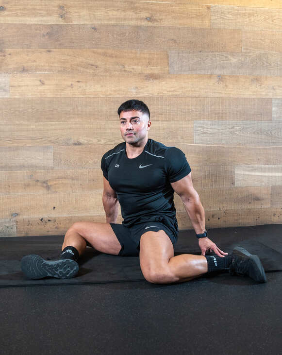 Part of the best full-body dumbbell workout: a man performing a 90 90 hip opener, sitting with legs at 90 degrees