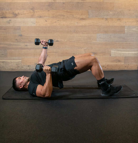 man in glute bridge alternating weight presses overhead