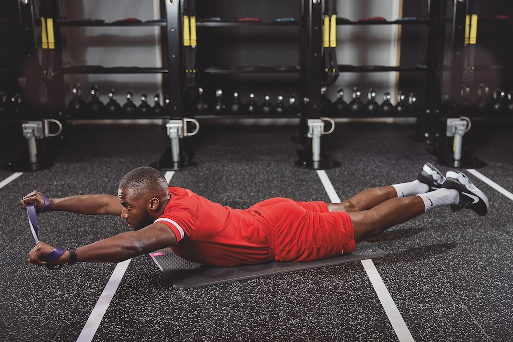 man in red top and red shorts doing a superman with banded row in the gym as part of a full-body circuit