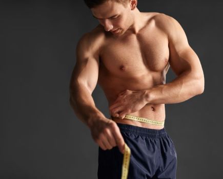 A shirtless man measuring his waist