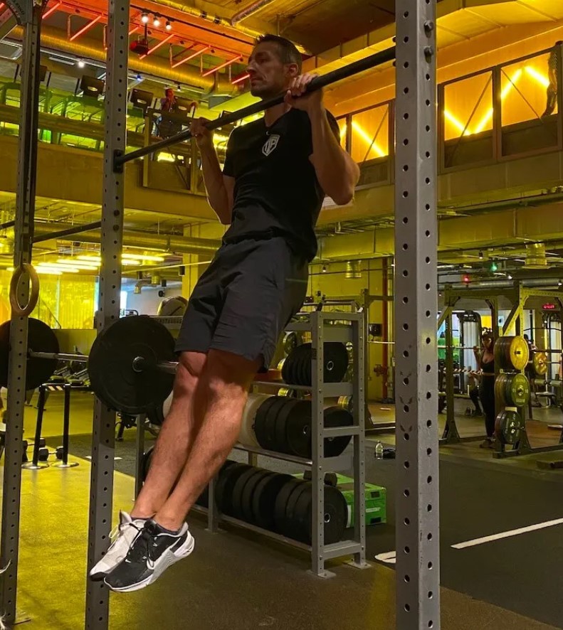 Man in a gym performing a bar pull-up