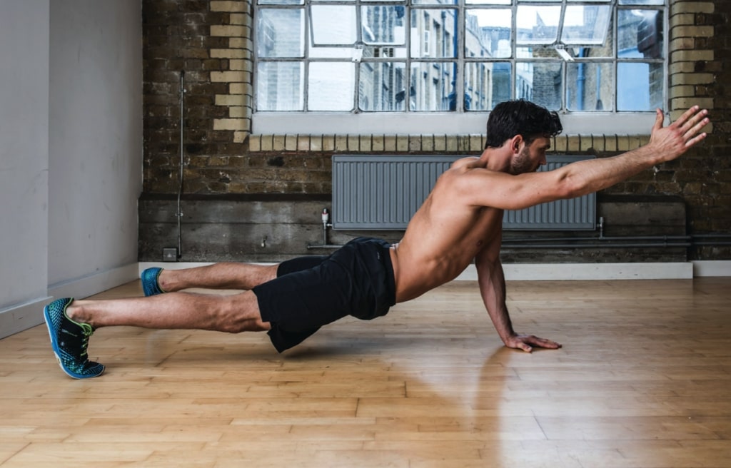 Man performing three-point reach plank variation