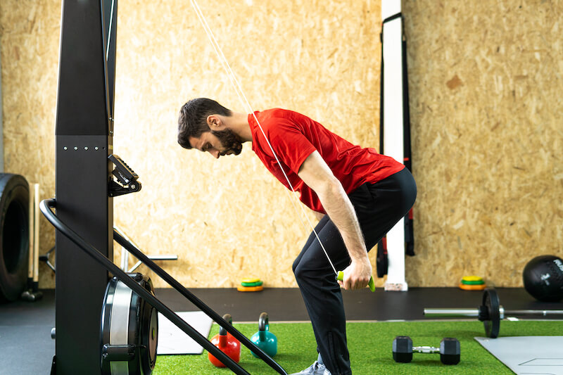 Man in red row and black bottoms using Concept2 SkiErg in gym
