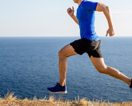 Close up of a man wearing running shorts running by the sea
