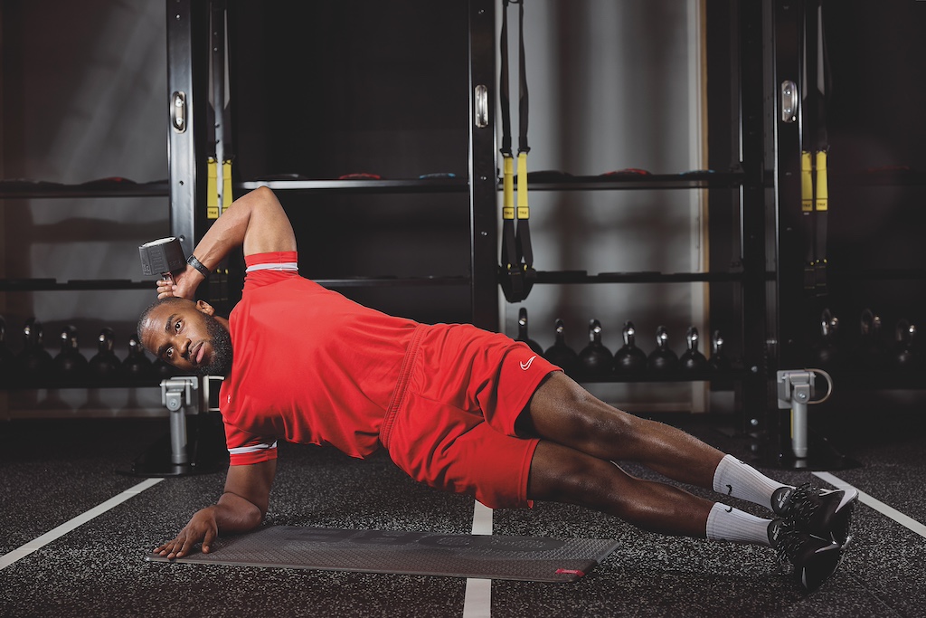 man in red top and red shorts doing a side plank with dumbbell triceps extension