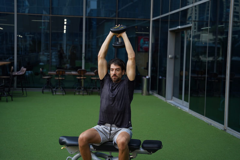 man demonstrating dumbbell overhead triceps extension