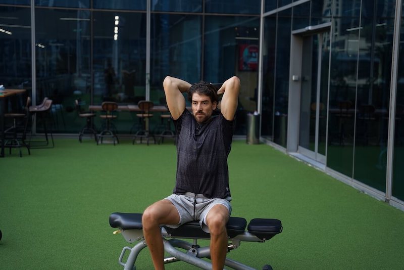 man demonstrating dumbbell overhead triceps extension with elbows bent